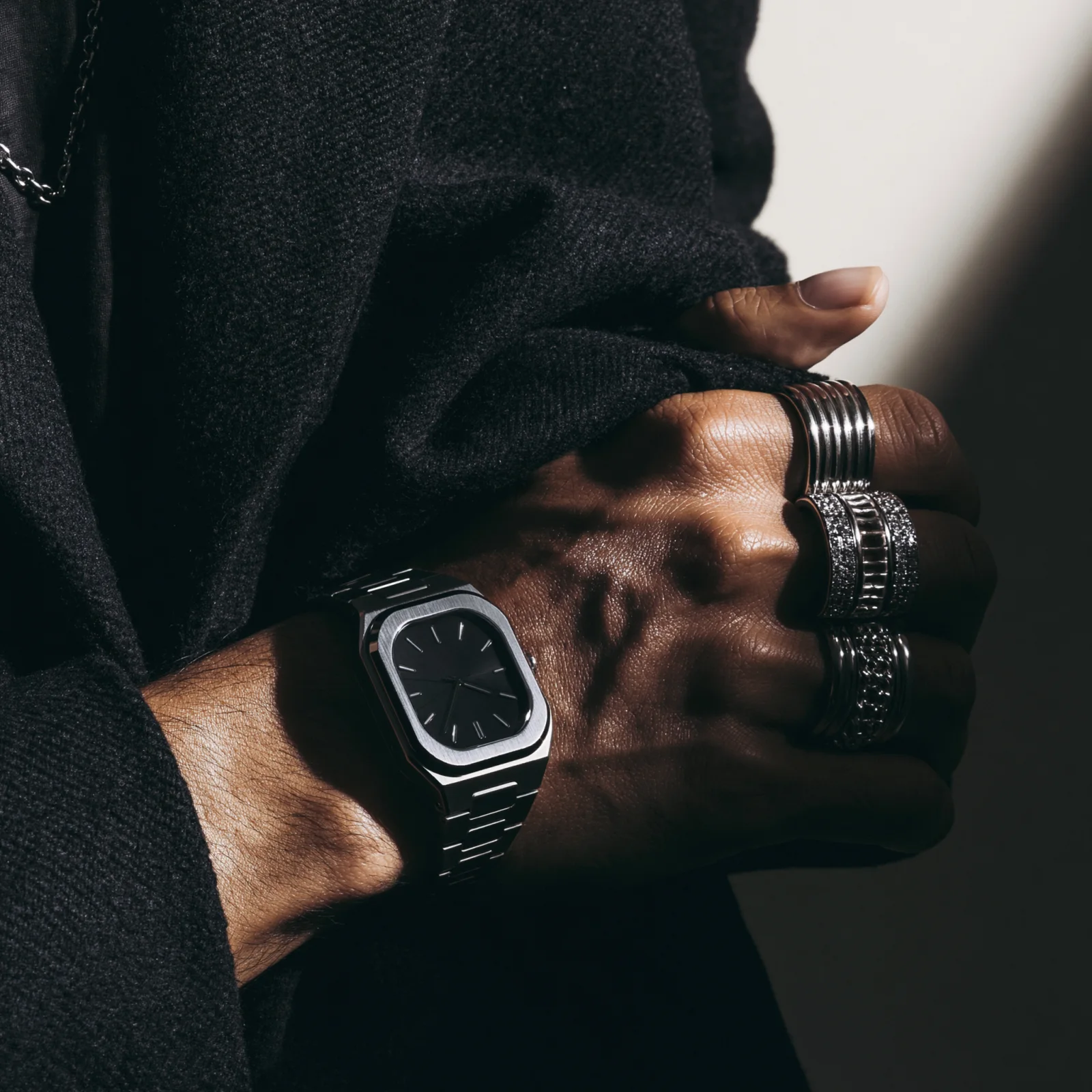 Macro flash editorial of an adult hand pulling a black watch over knitwear