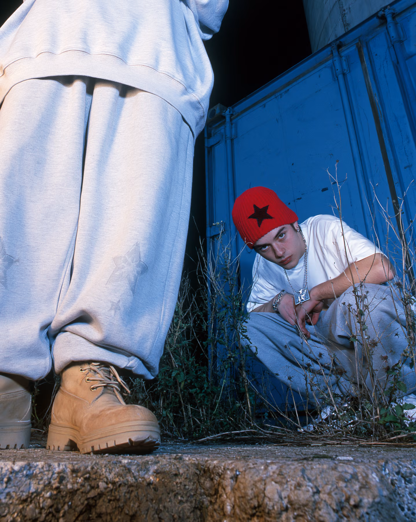 Low-angle streetwear editorial with blue container and red beanie