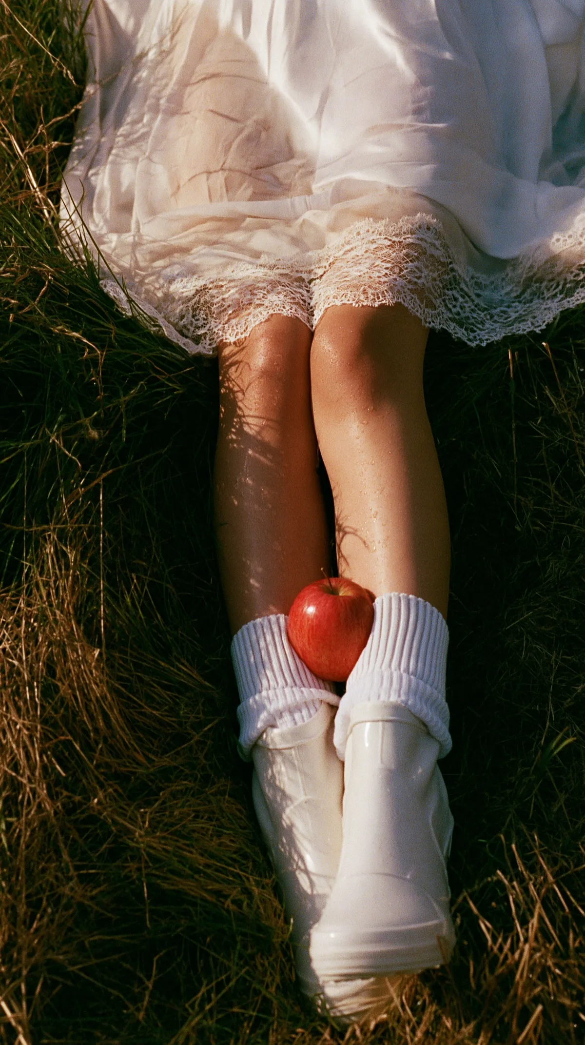 Intimate fashion detail in tall grass with white boots and red apple