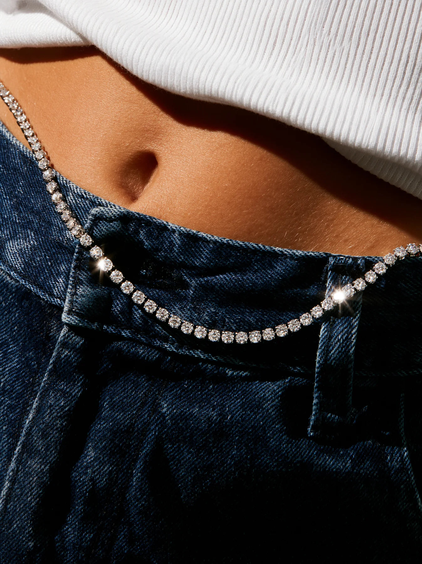 Fashion jewelry editorial with diamond necklace draped across denim waist