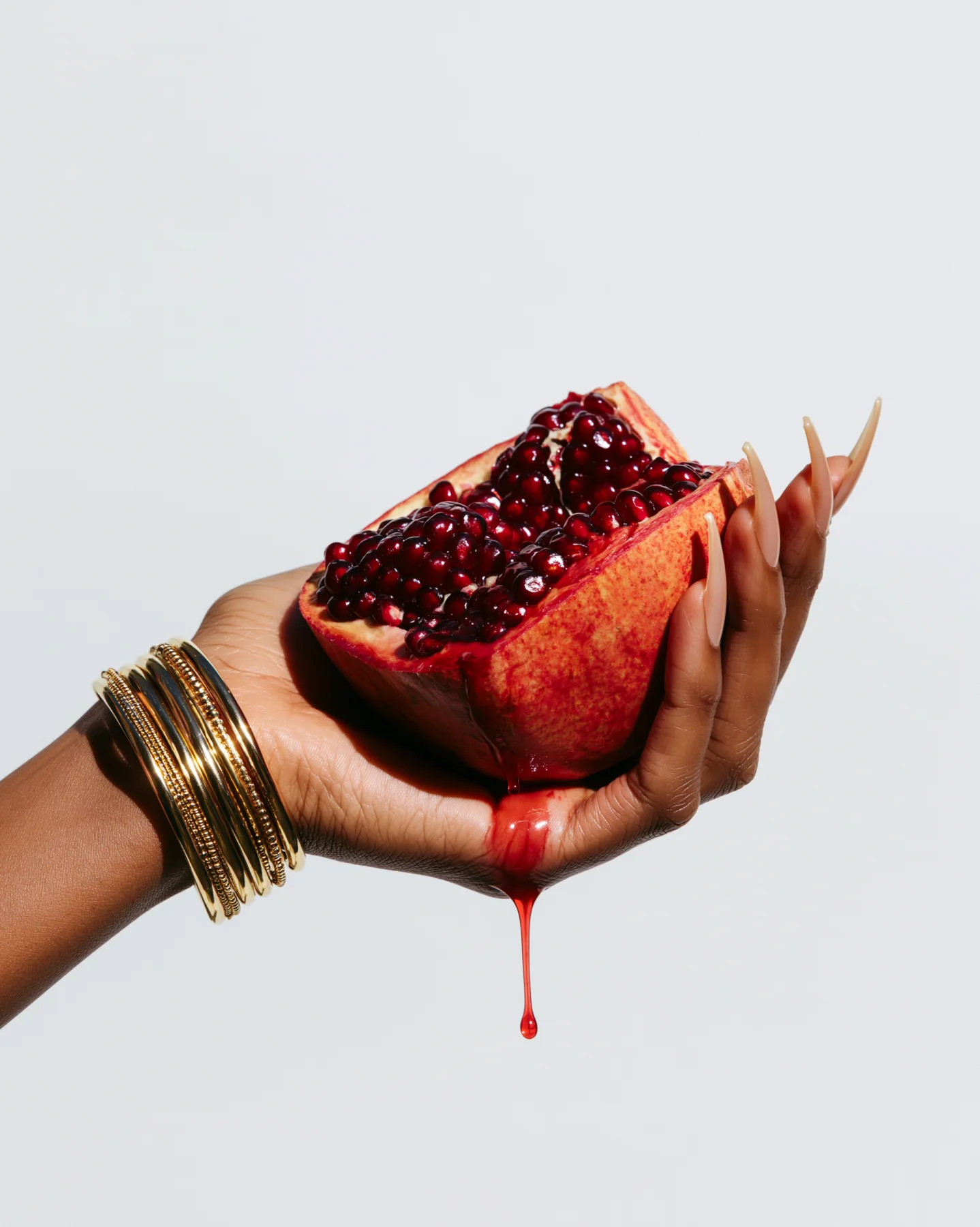 Close-up campaign image of a hand holding jewelry near pomegranate red tones